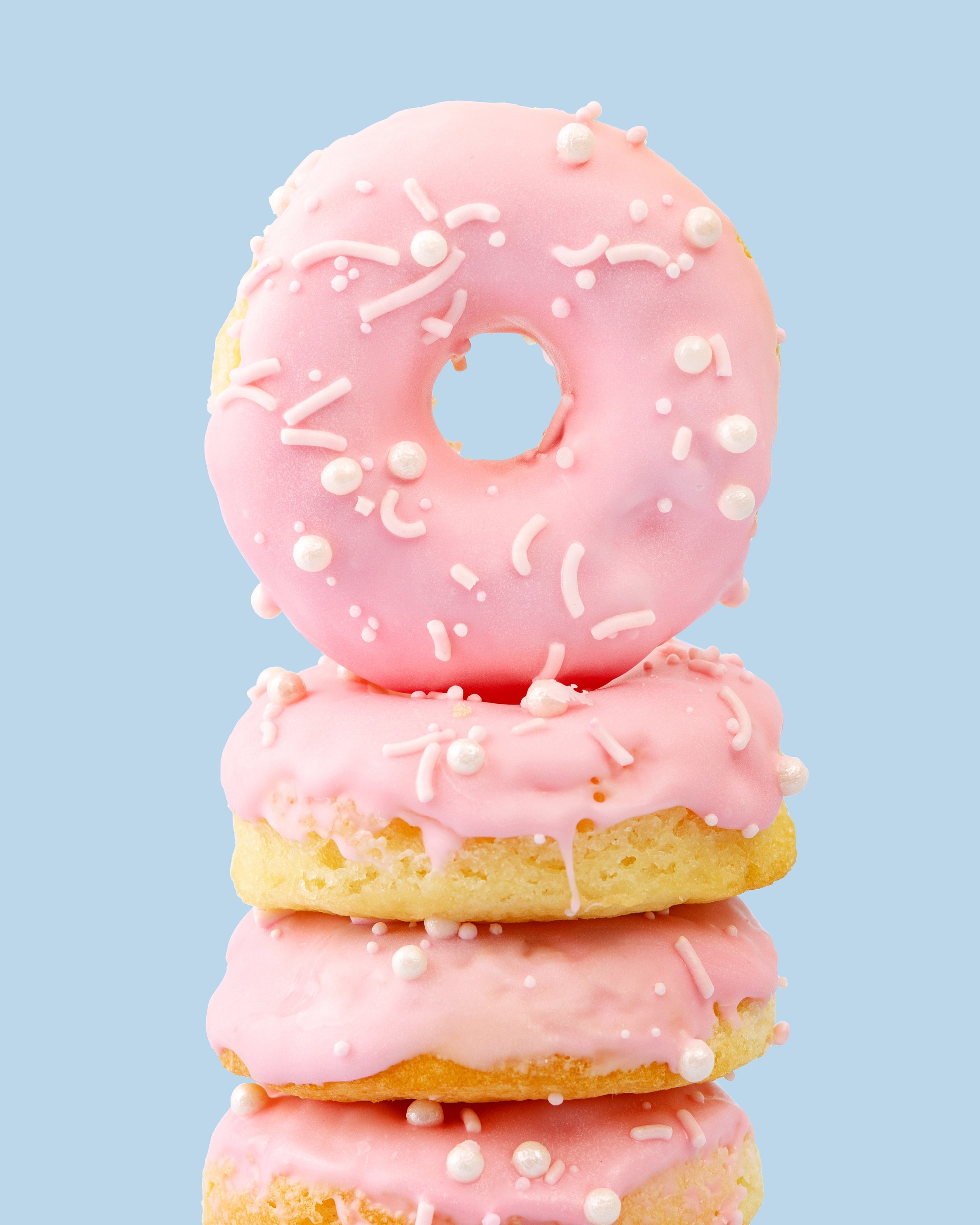 Lifestyle image of pink glazed Sweetshop Vanilla Cake Donuts with white sprinkles