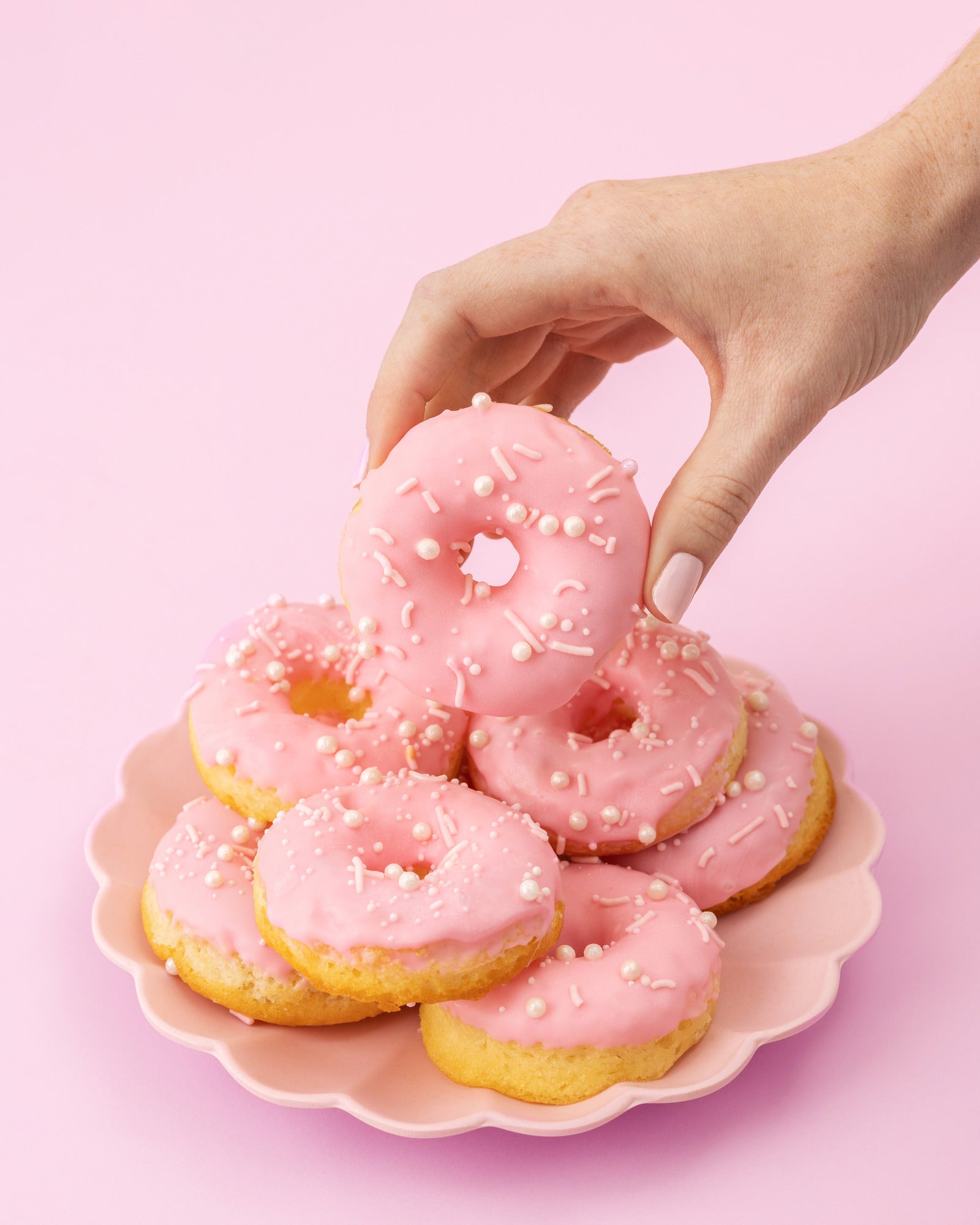 Lifestyle images of person picking up pink glazed Sweetshop Vanilla Cake Donuts