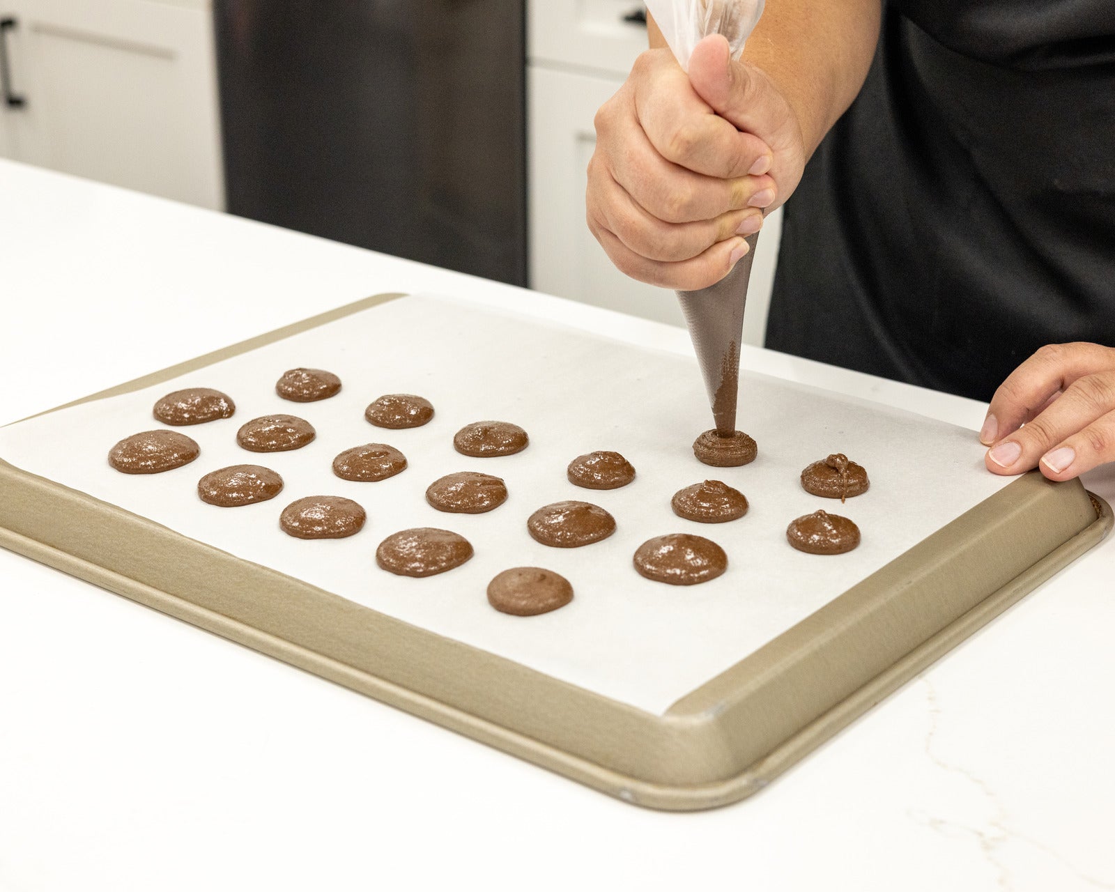 Lifestyle image of someone putting mixed macaron mix on baking sheet