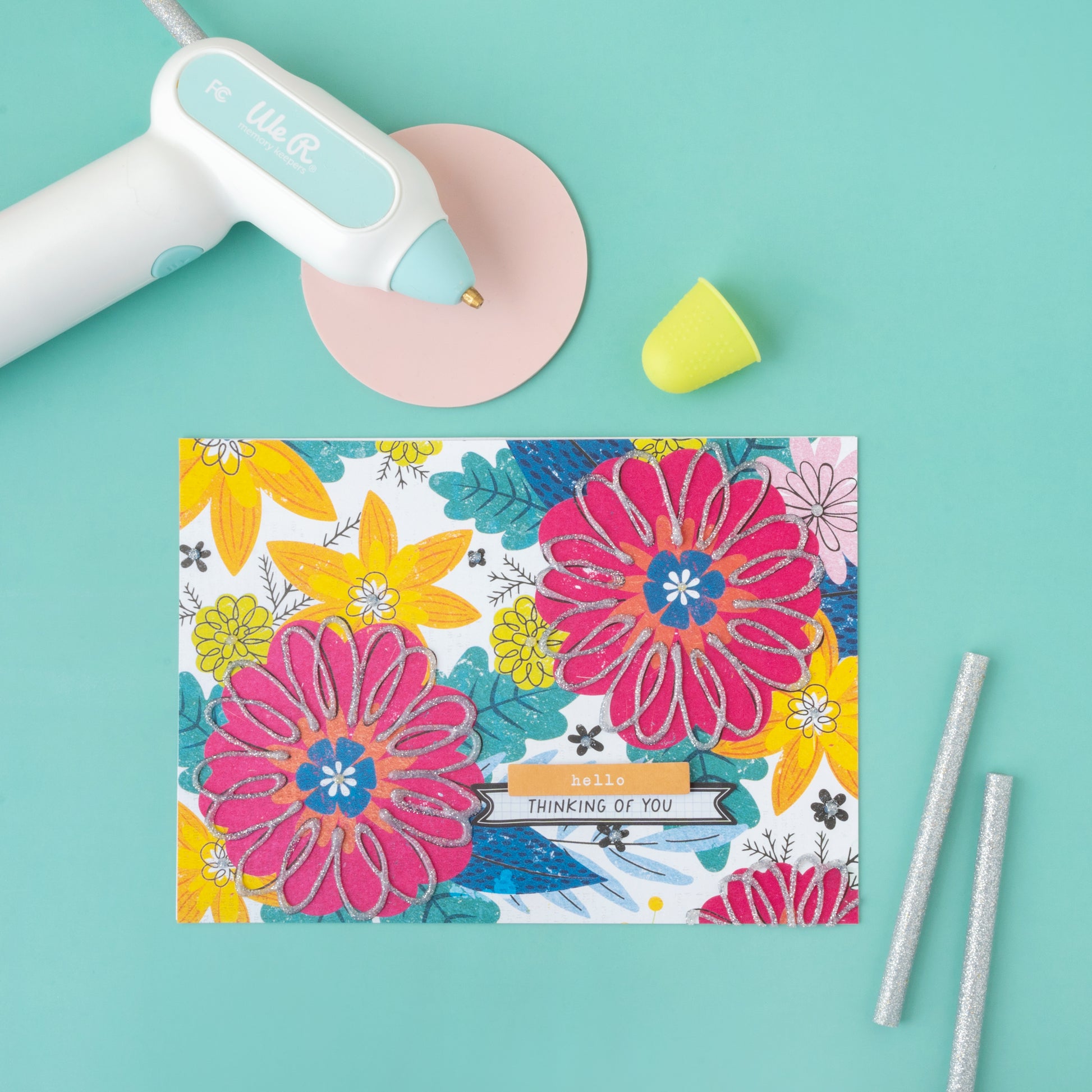 Lifestyle image of a card and the We R Makers Creative Flow Glue gun with glitter glue sticks