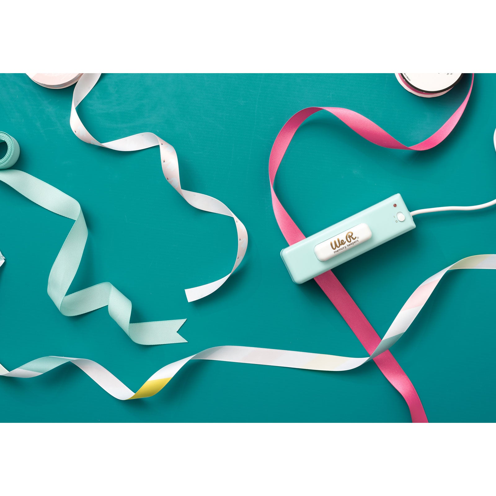 Lifestyle image of We R Makers USB Ribbon Cutter surrounded with ribbon