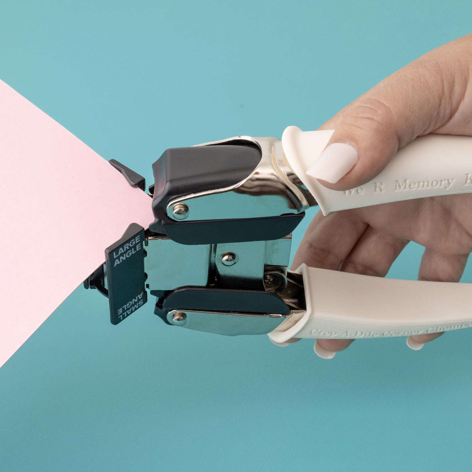 Lifestyle image of We R Makers Crop-A-Dile Small & Large Angle Corner Chomper Punch being used on corner of pink craft paper