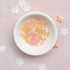 White bowl with pink and yellow flower-shaped objects on a pink background with white flowers.