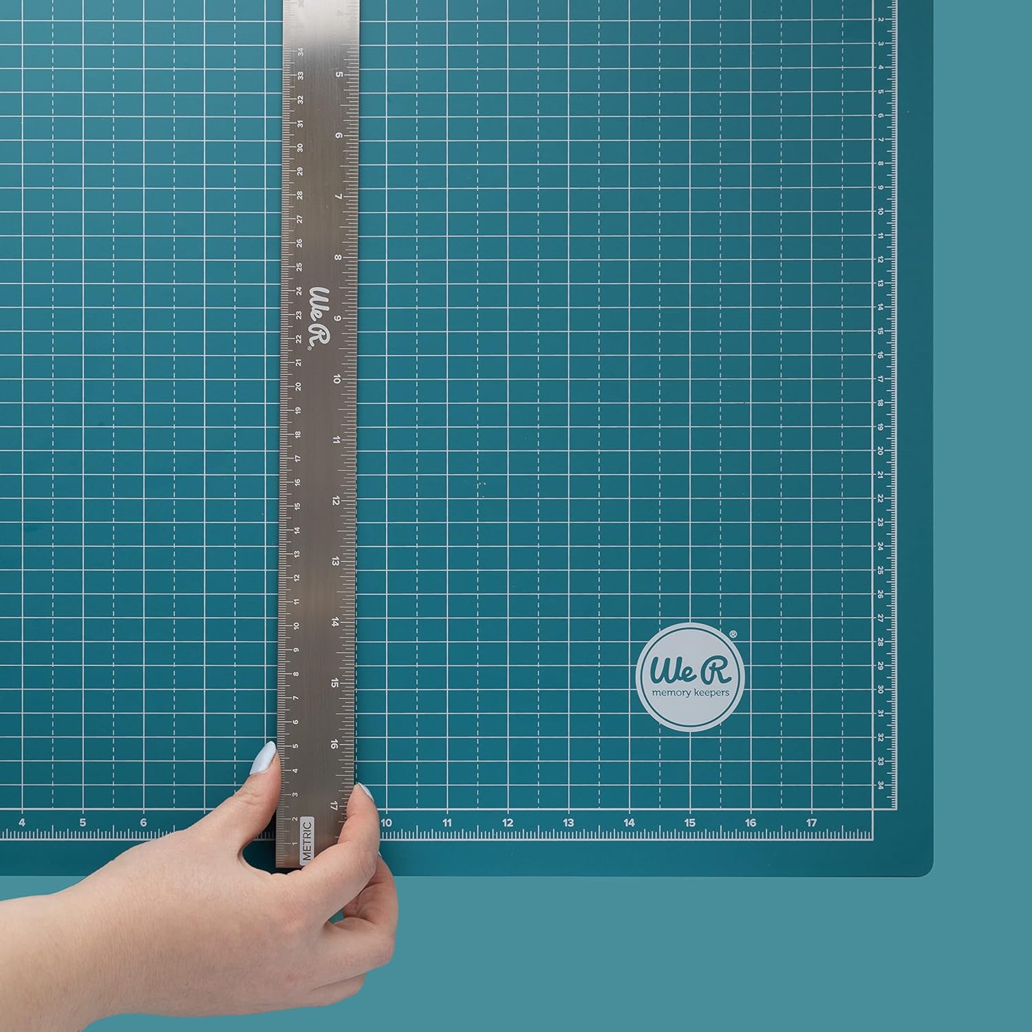 A person using a ruler on the We R Makers Large 18x14 Magnetic Mat.