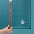 A person using a ruler on the We R Makers Large 18x14 Magnetic Mat.