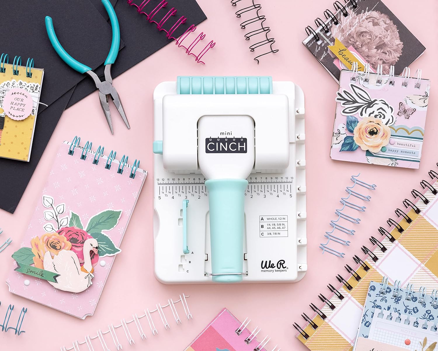 We R Makers Mini Cinch Book Binding Machine surrounding by an assortment of bound notebooks