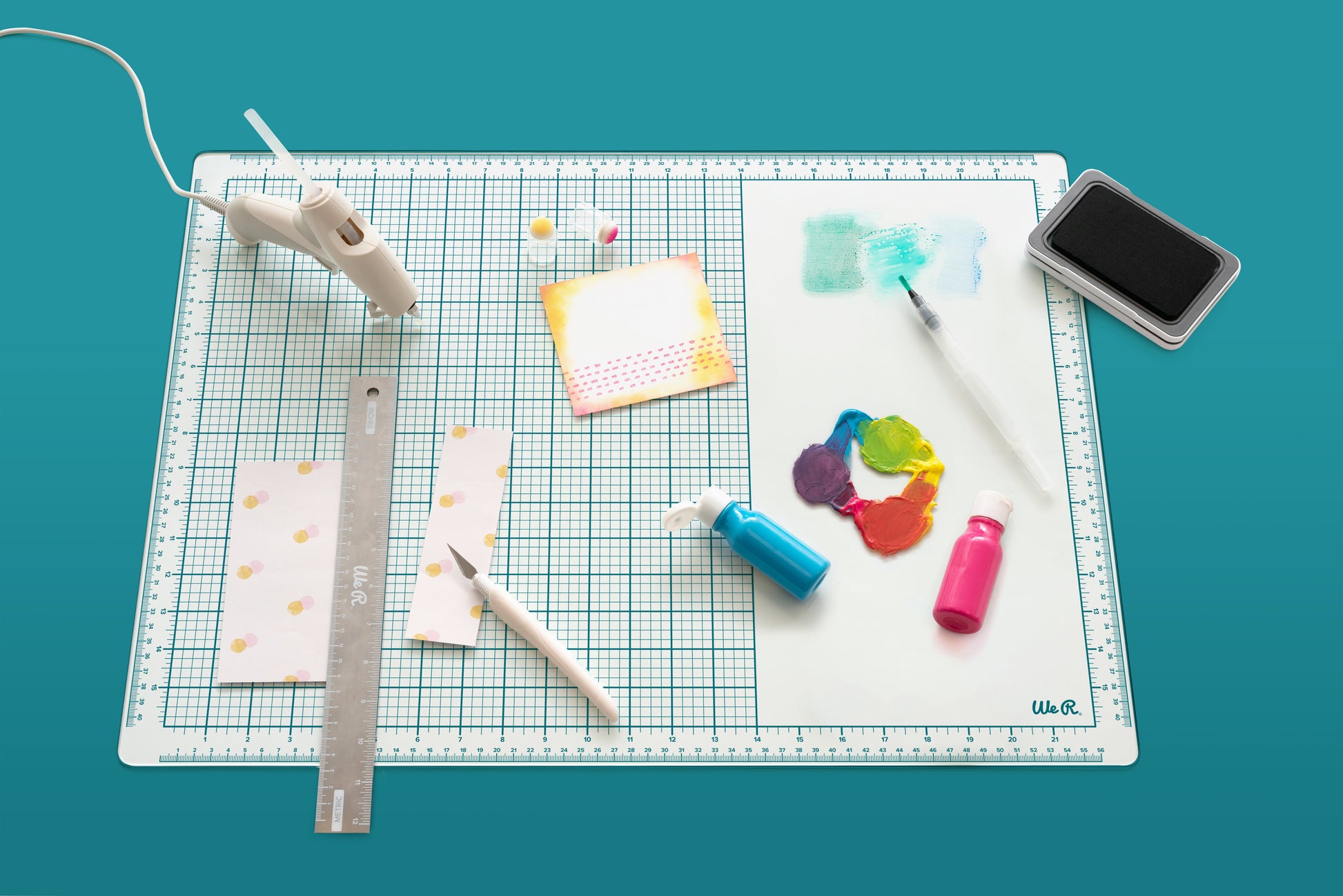 Picture of some crafts like paint, glue gun, ruler, and other items on the We R Makers Mixed Media 16x22 Glass Mat.